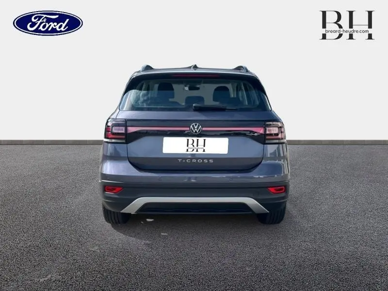 Vue arrière d'un Volkswagen T-Cross gris cendré métallisé avec feux arrière reliés par un bandeau lumineux noir.