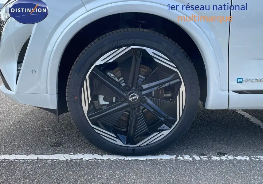 Gros plan sur la roue avant gauche du Nissan Qashqai blanc nacré avec jante noire et détails argentés.