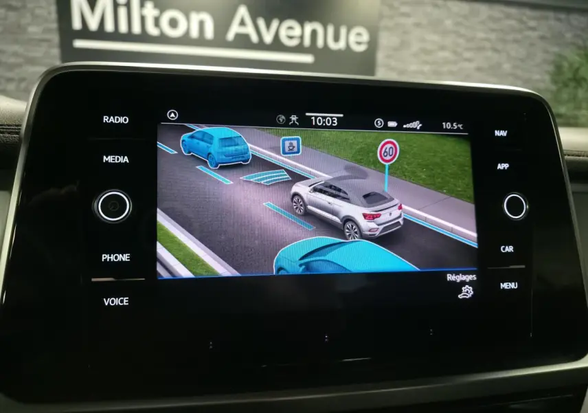 Écran tactile intérieur montrant l'assistance de conduite avec un Volkswagen T-Roc gris vu de trois quarts arrière droit.