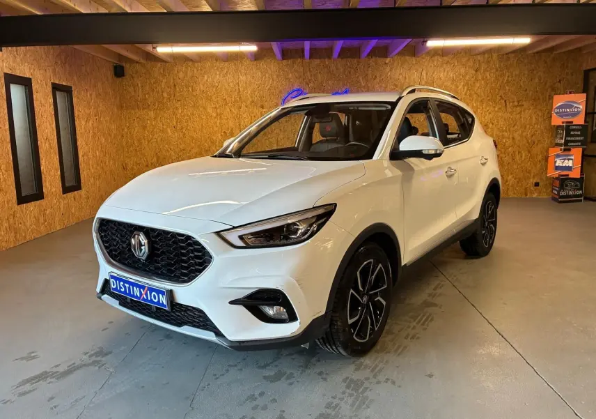 Vue 3/4 avant d’un MG ZS blanc 2022 dans un intérieur en bois, avec calandre noire et jantes noires distinctives.