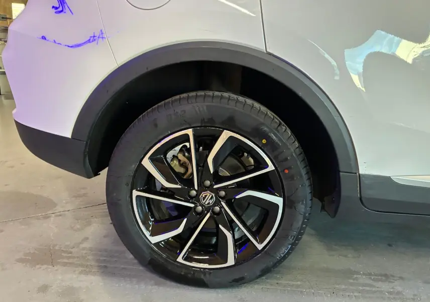 Gros plan sur la roue arrière droite du MG ZS blanc, mettant en valeur la jante noire et argentée au design moderne.