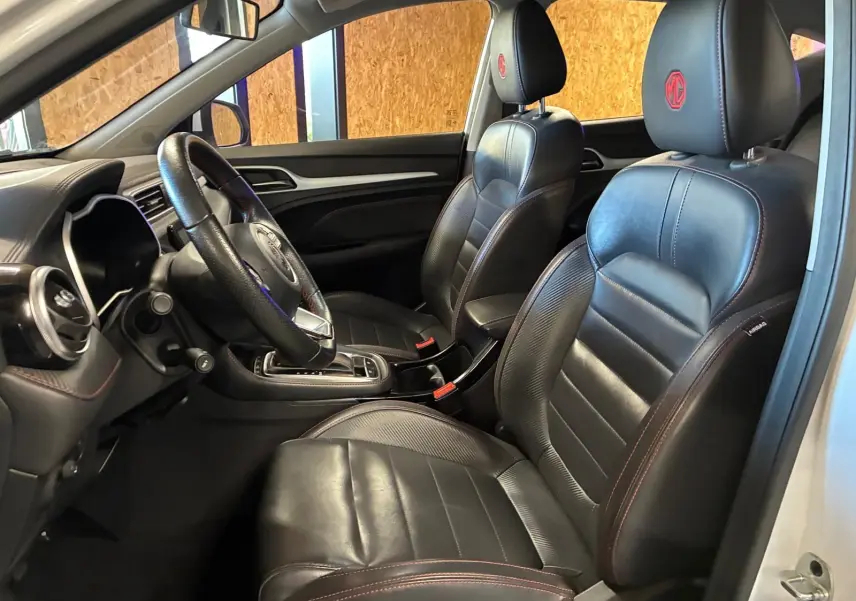 Vue intérieure côté gauche du MG ZS blanc 2022, sièges cuir noirs avec logo MG rouge brodé sur les appuie-têtes.