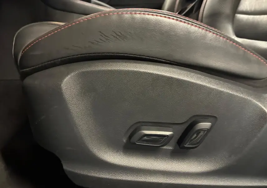 Gros plan sur les commandes de réglage électrique du siège avant en cuir noir avec surpiqûres rouges du MG ZS blanc.