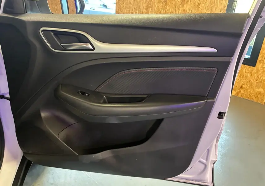 Vue intérieure de la porte avant gauche du MG ZS blanc, avec garniture noire et surpiqûres rouges visibles.