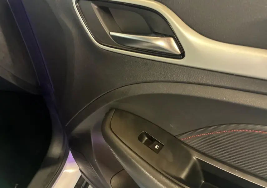 Gros plan sur la poignée intérieure et le panneau de porte côté gauche du MG ZS blanc, avec surpiqûres rouges décoratives.