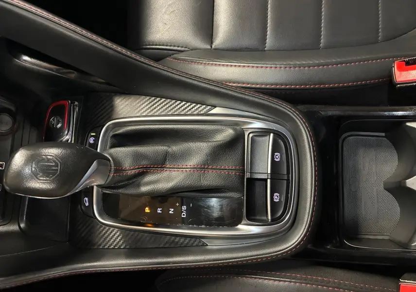 Vue rapprochée de la console centrale noire avec levier de vitesse cuir et surpiqûres rouges du MG ZS blanc 2022.