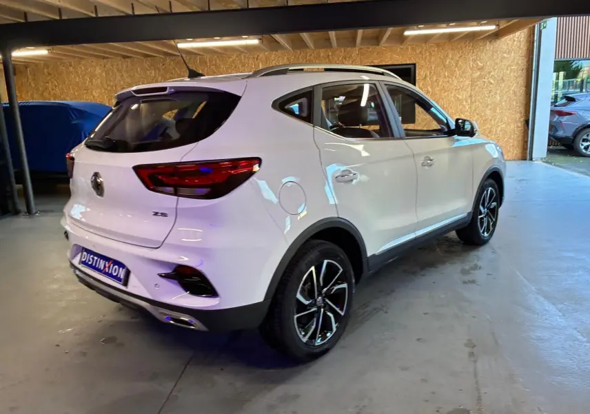 Vue 3/4 arrière droite du SUV blanc MG ZS 2022, avec jantes noires et détails chromés, stationné en intérieur.