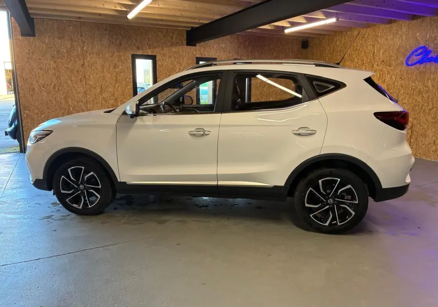 Vue de profil côté gauche d’un MG ZS blanc 2022 avec jantes alliage noires et toit ouvrant en intérieur bois.