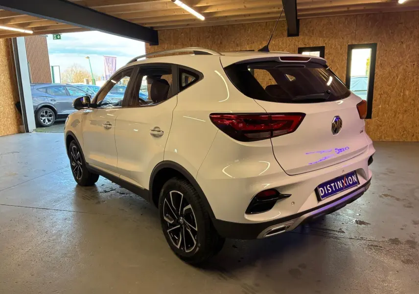 Vue 3/4 arrière droite d’un MG ZS blanc 2022 dans un garage, avec jantes noires et détails chromés.
