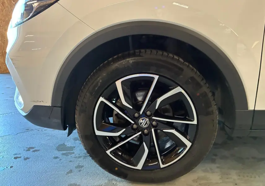 Gros plan sur la roue avant gauche noire et argentée du MG ZS blanc, mettant en valeur la jante au design moderne.