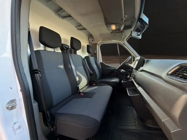 Vue intérieure côté conducteur du Renault Master blanc 2023, montrant les sièges tissu noir et gris et le tableau de bord.