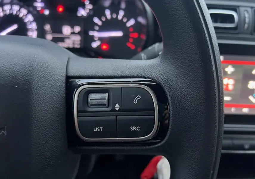 Gros plan sur les commandes audio au volant à gauche du Citroën C3 Shine 2023, intérieur noir avec tableau de bord flou.