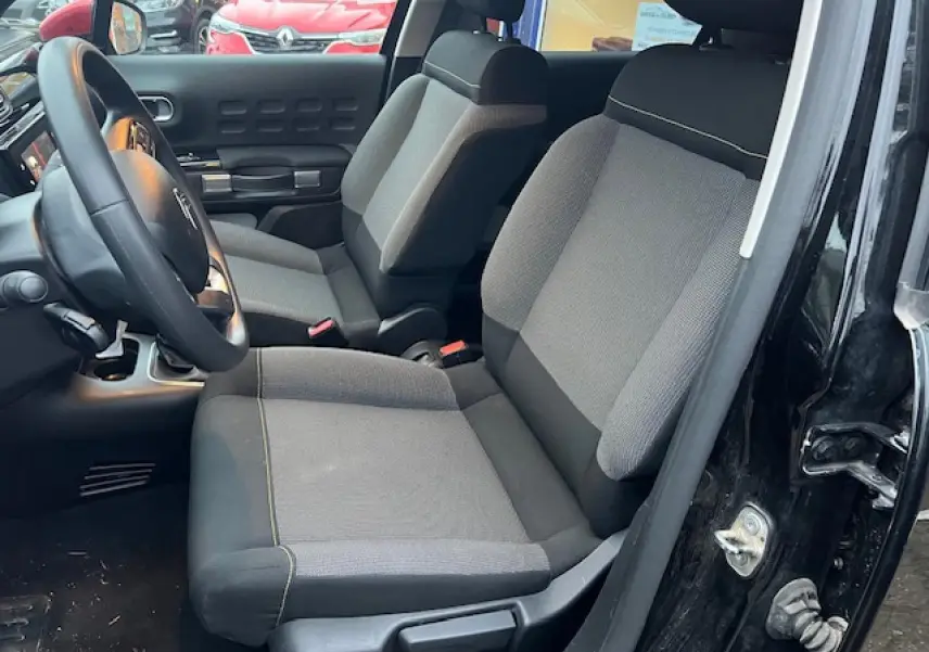 Vue intérieure côté conducteur de la Citroën C3 Shine 2023 noire toit rouge, sièges tissu gris et noir, volant multifonction.