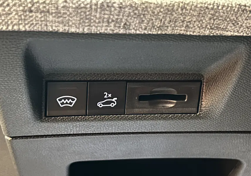 Gros plan sur les commandes intérieures noires du Peugeot 3008 blanc Okenite, avec bouton ouverture hayon et dégivrage.