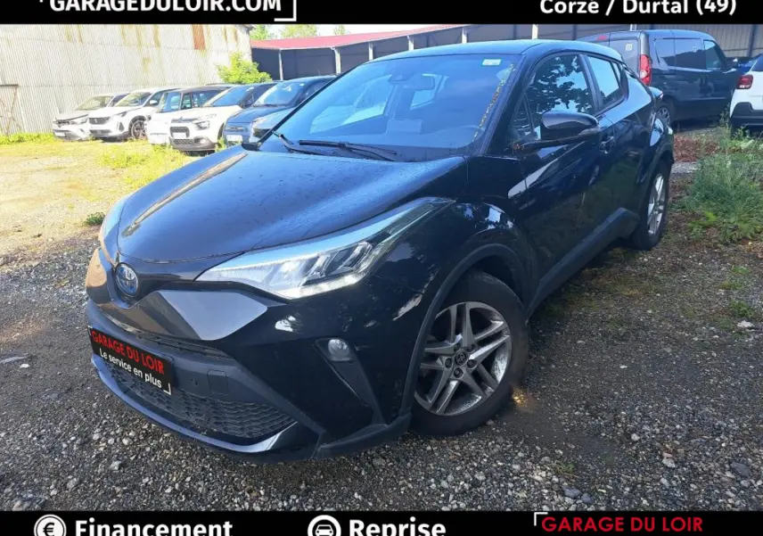 Vue 3/4 avant d'une Toyota C-HR 1.8 Hybride noire avec jantes alliage, garée sur un sol gravillonné.