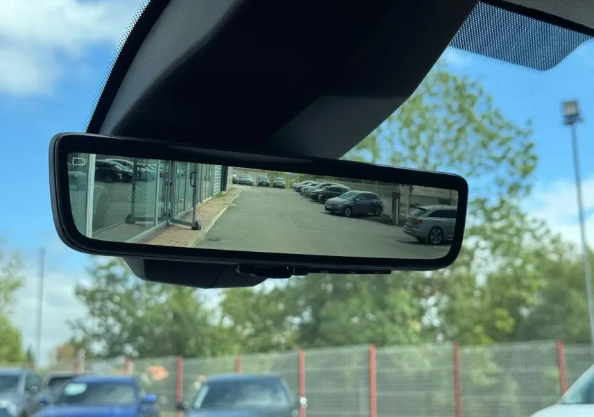 Rétroviseur intérieur numérique montrant une vue arrière dégagée d’un parking sous ciel bleu.