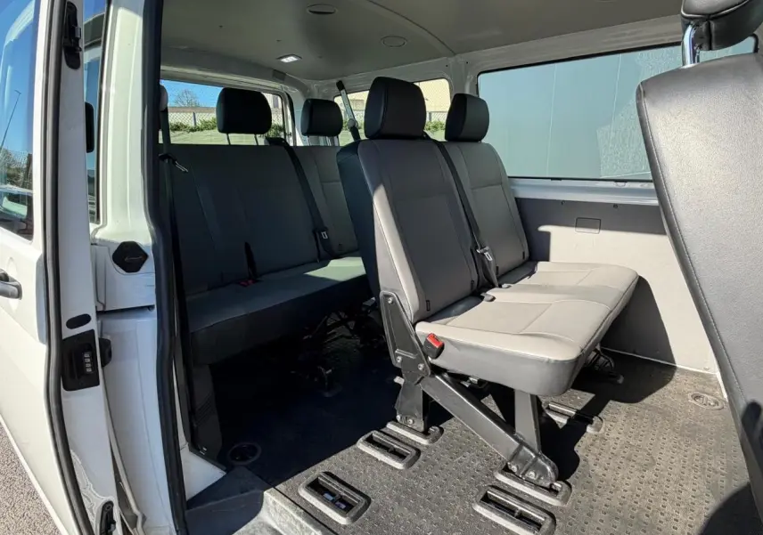 Vue intérieure côté droit du Volkswagen Transporter T6 Minibus blanc, montrant les sièges passagers en rangées.