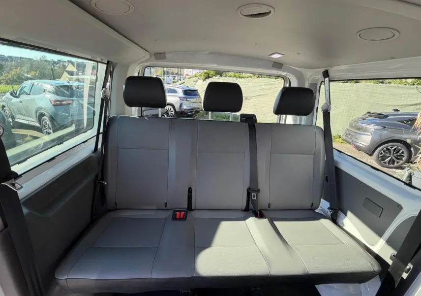 Banquette arrière grise vue de face à l'intérieur du Volkswagen Transporter T6 Minibus blanc, avec ceintures de sécurité visibles.