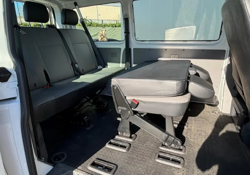 Vue intérieure côté droit du Volkswagen Transporter T6 Minibus blanc, montrant les sièges arrière et une banquette rabattue.