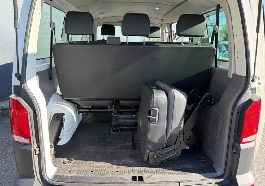 Vue arrière ouverte du Volkswagen Transporter T6 Minibus blanc, montrant les sièges rabattus et l'espace de chargement intérieur.