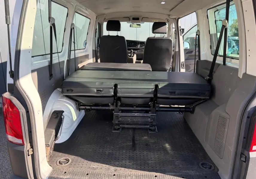 Intérieur arrière du Volkswagen Transporter T6 blanc, vue de la porte ouverte avec banquette rabattue et espace de chargement visible.