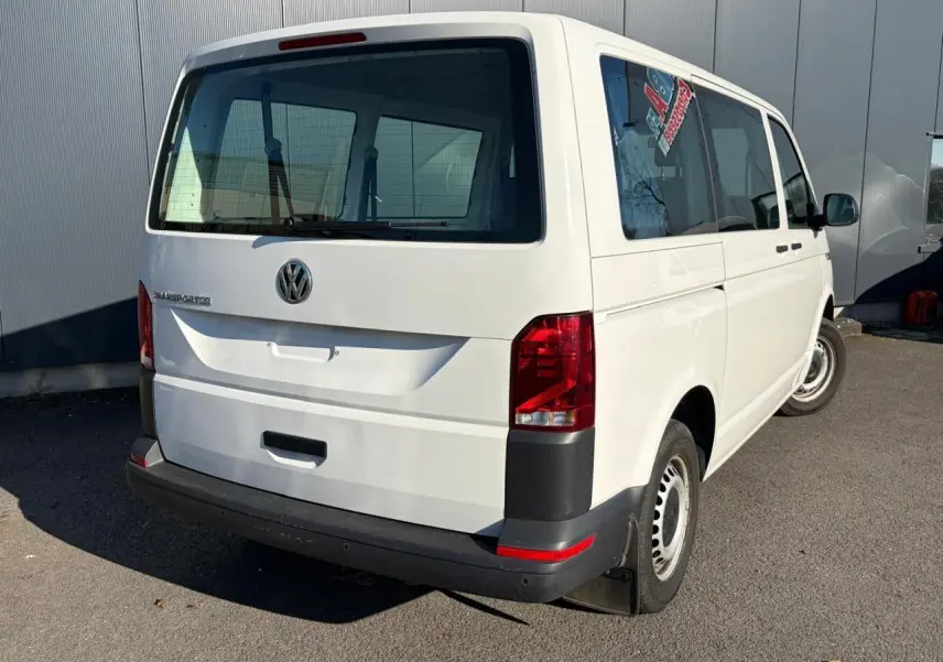 Vue 3/4 arrière droite d'un Volkswagen Transporter T6 Minibus blanc avec vitres teintées et feux arrière rouges.