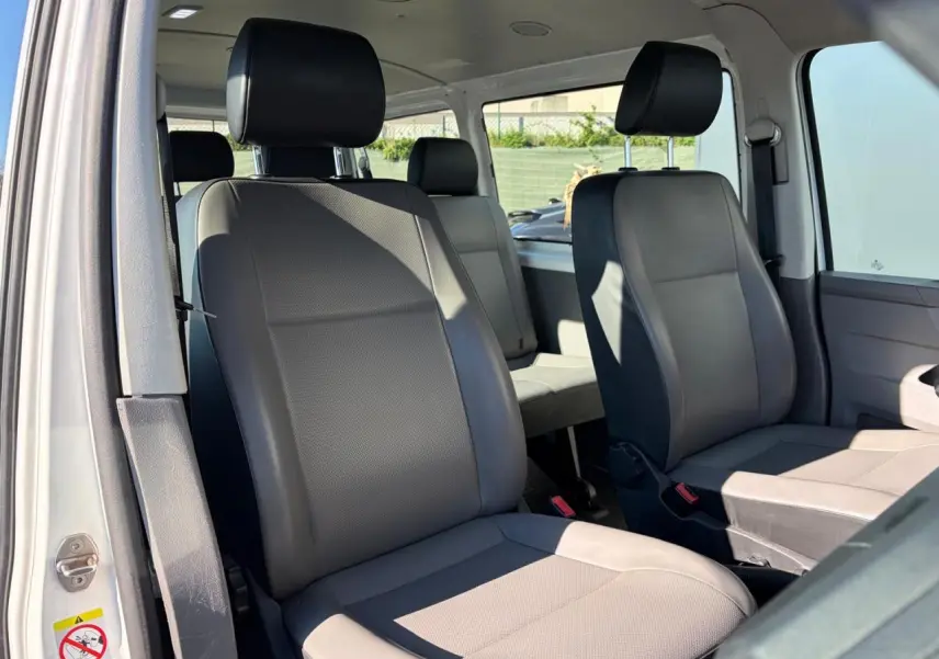 Vue intérieure côté droit du Volkswagen Transporter T6 Minibus blanc, montrant les sièges avant et arrière en tissu gris.