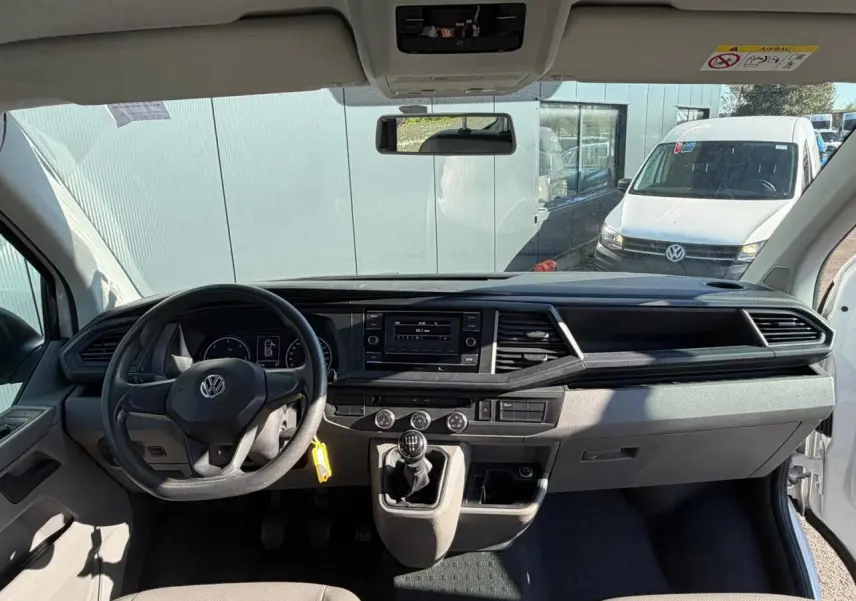 Vue intérieure avant du Volkswagen Transporter T6 Minibus blanc, montrant le tableau de bord et la boîte manuelle.