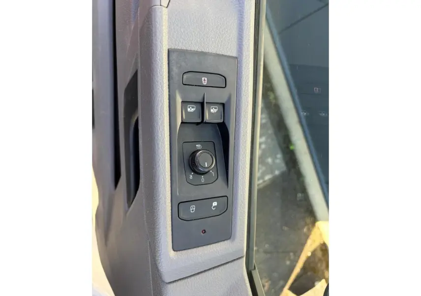 Gros plan sur les commandes des rétroviseurs et des vitres côté conducteur du Volkswagen Transporter T6 blanc.