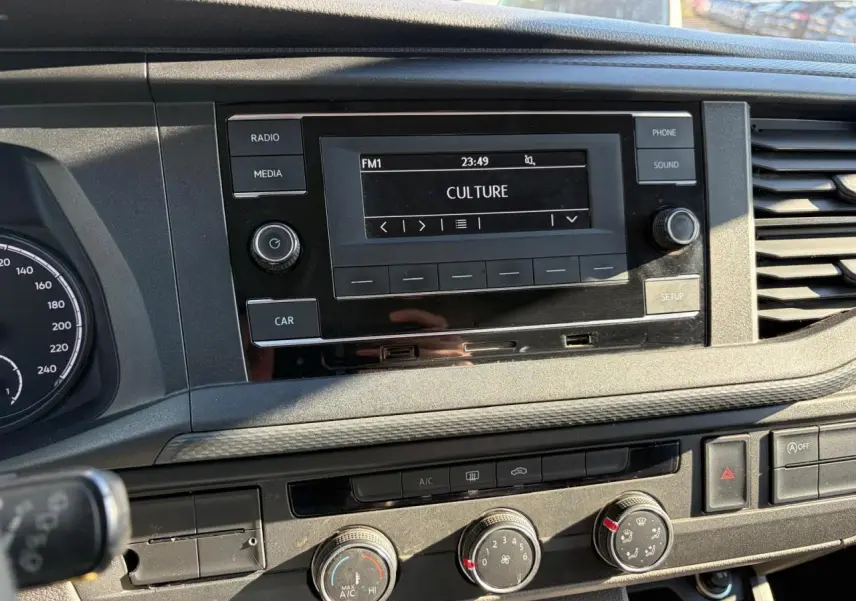 Gros plan sur la console centrale du Volkswagen Transporter T6 blanc, avec écran radio et commandes de climatisation visibles.