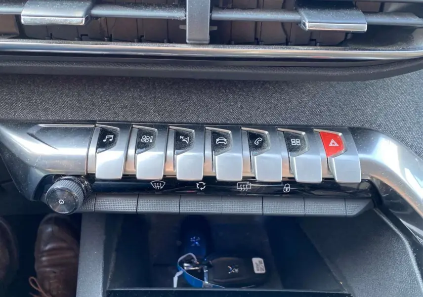 Gros plan sur la rangée de boutons argentés et noir du tableau de bord du Peugeot 3008 blanc, avec clé visible dessous.