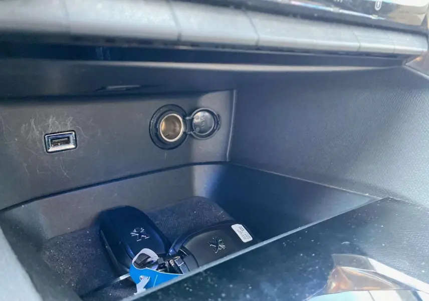 Gros plan sur la boîte à gants ouverte du Peugeot 3008 blanc, montrant deux clés et une prise USB.