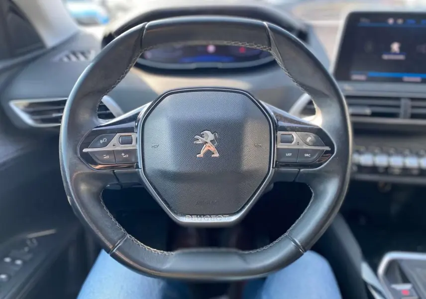 Vue rapprochée du volant cuir noir du Peugeot 3008 2018 avec commandes intégrées et tableau de bord flou en arrière-plan.