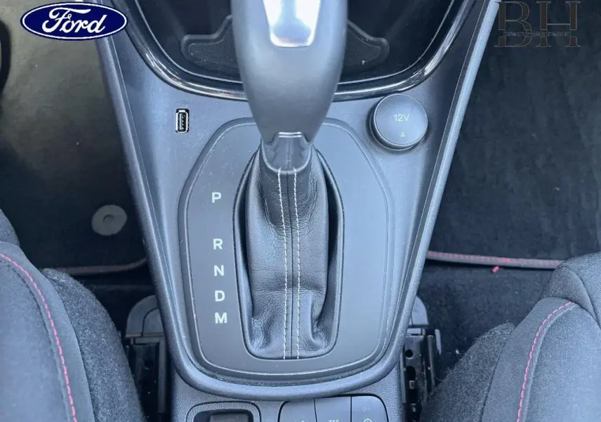 Gros plan sur la console centrale de la Ford Puma 2022, boîte auto avec levier cuir et coutures blanches, sièges tissu noir à surpiqûres rouges.