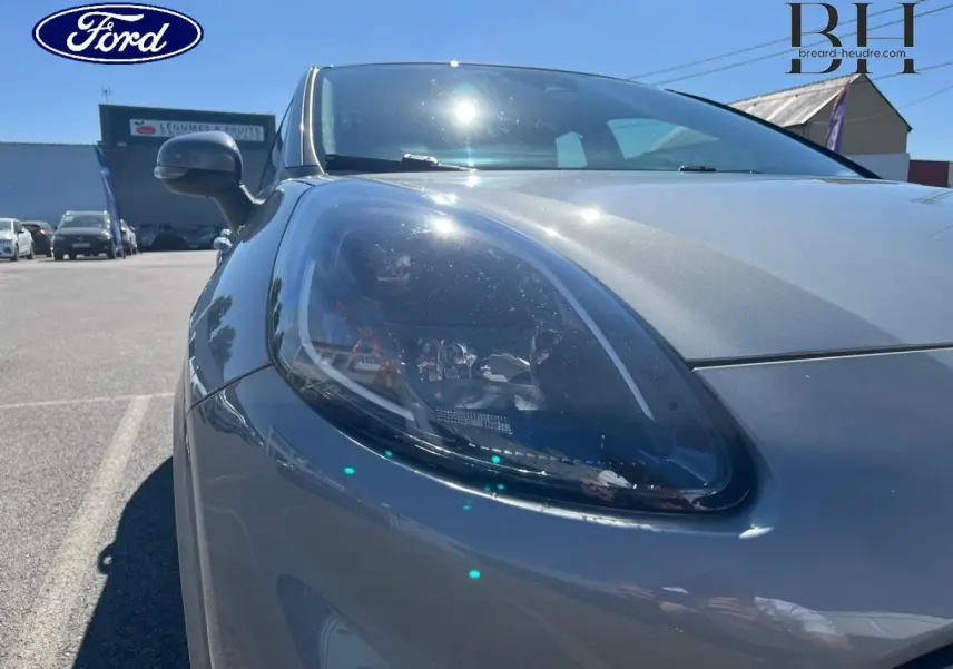 Gros plan sur le phare avant gauche du Ford Puma gris Solar métallisé sous un ciel ensoleillé.
