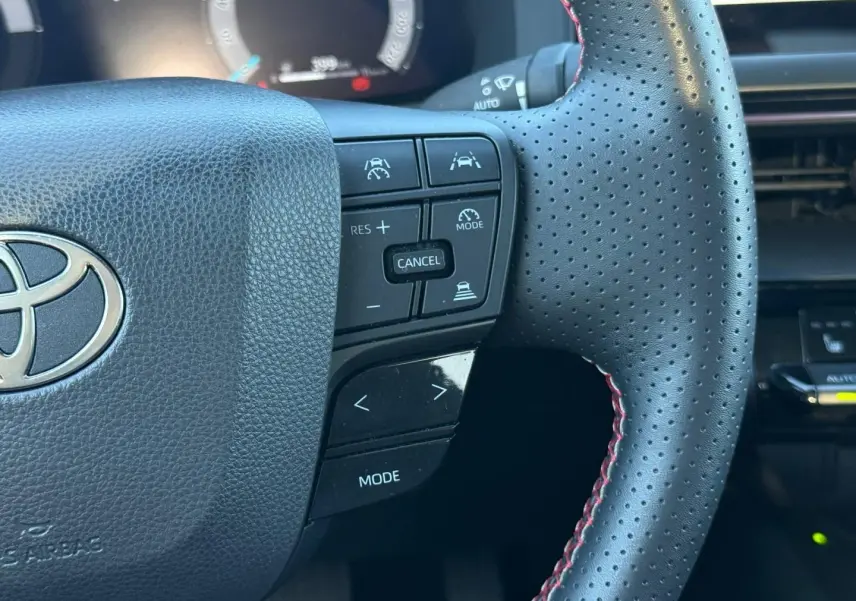 Gros plan sur le volant perforé noir avec surpiqûres rouges du Toyota C-HR 2.0 Hybride GR Sport 2025, boutons multifonctions visibles.