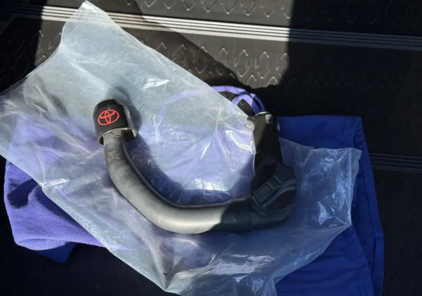 Gros plan sur un attelage de remorque noir avec logo Toyota rouge, posé sur un tissu bleu dans un coffre.