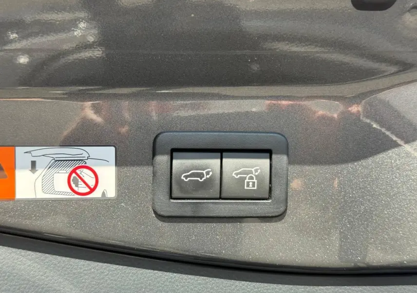 Gros plan sur les boutons d'ouverture et de verrouillage du coffre sur la garniture gris atlas métallisé du Toyota C-HR 2025.
