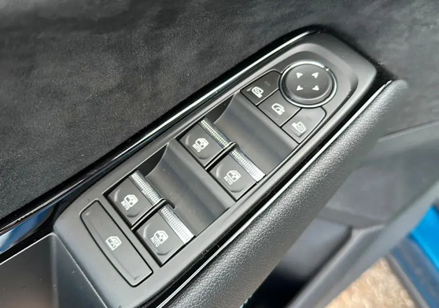 Gros plan sur les commandes des vitres électriques côté gauche d'une Renault Austral bleu outremer, avec boutons noirs et finition cuir.