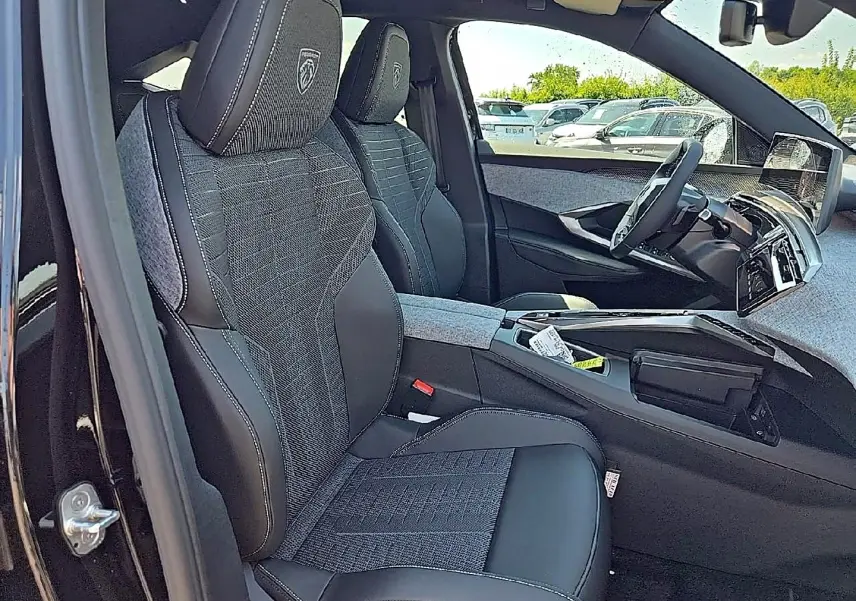 Vue intérieure côté gauche du Peugeot 3008 noir 2026, sièges tissu et cuir avec logo Peugeot brodé sur appuie-tête.