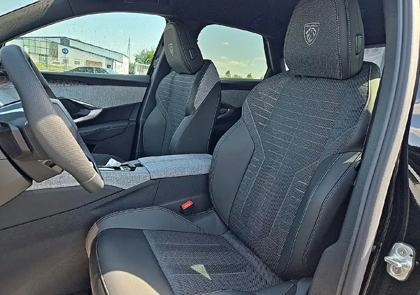 Vue intérieure côté conducteur du Peugeot 3008 noir 2026, sièges tissu et cuir avec logo Peugeot brodé sur appuie-tête.