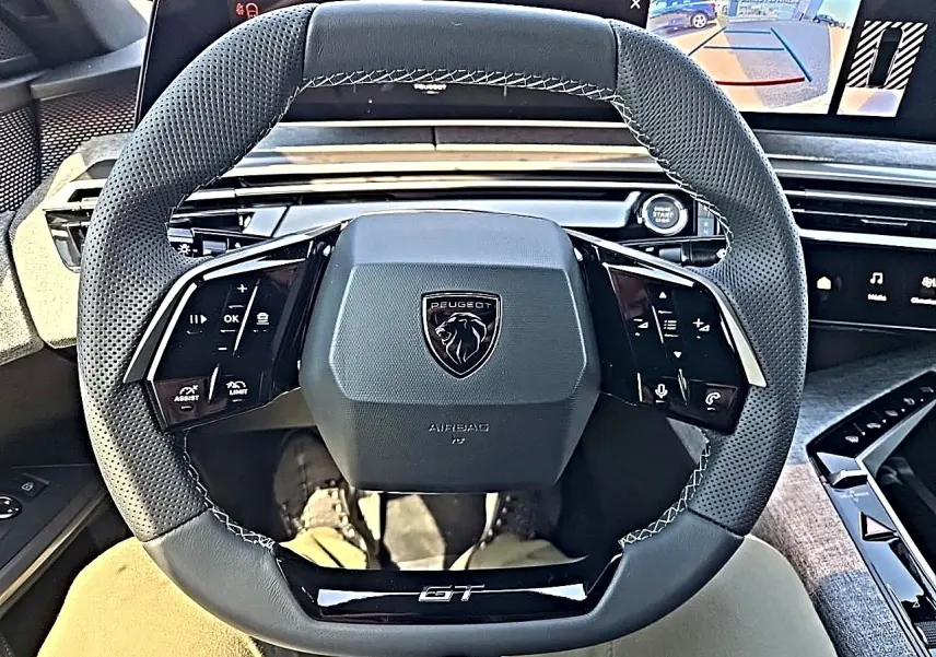 Vue intérieure centrée sur le volant cuir noir perforé du Peugeot 3008 1.2 hybrid GT avec commandes multifonctions et logo GT.