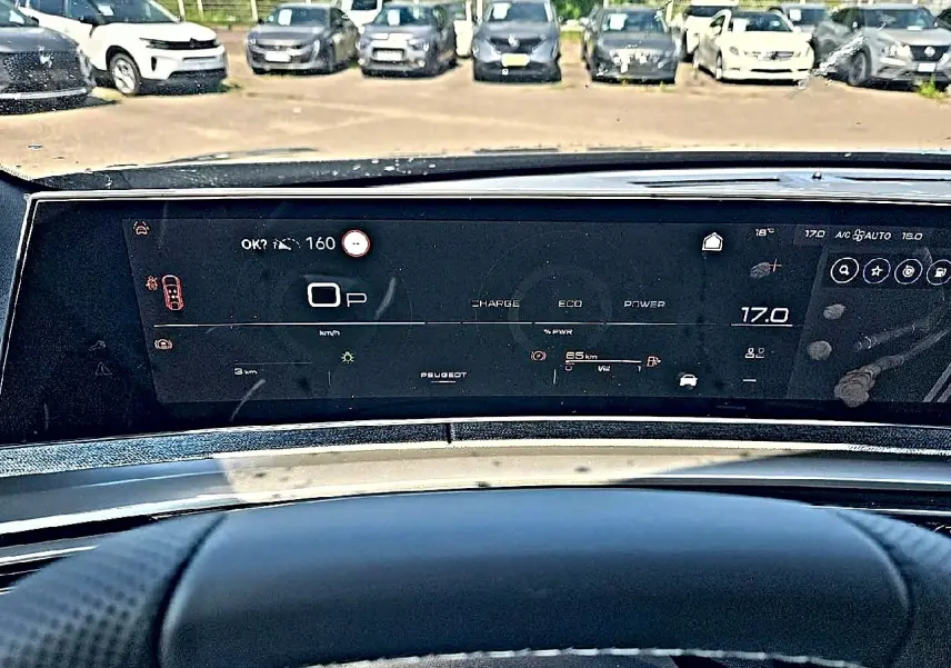 Vue intérieure du tableau de bord numérique du Peugeot 3008 noir, affichant la vitesse et la température, avec parking en arrière-plan.