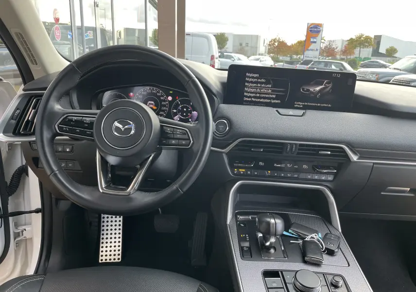 Vue intérieure du tableau de bord et volant noir du Mazda CX-60 blanc nacré, avec écran tactile et console centrale moderne.