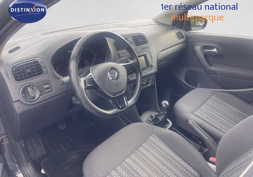 Vue intérieure côté conducteur de la Volkswagen Polo noire 2016, montrant le volant, la boîte manuelle et les sièges tissu gris.