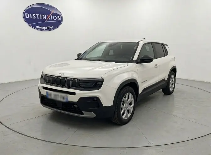 Jeep Avenger blanc en 3/4 avant droit, avec calandre noire distinctive et jantes argentées, sur fond neutre intérieur.