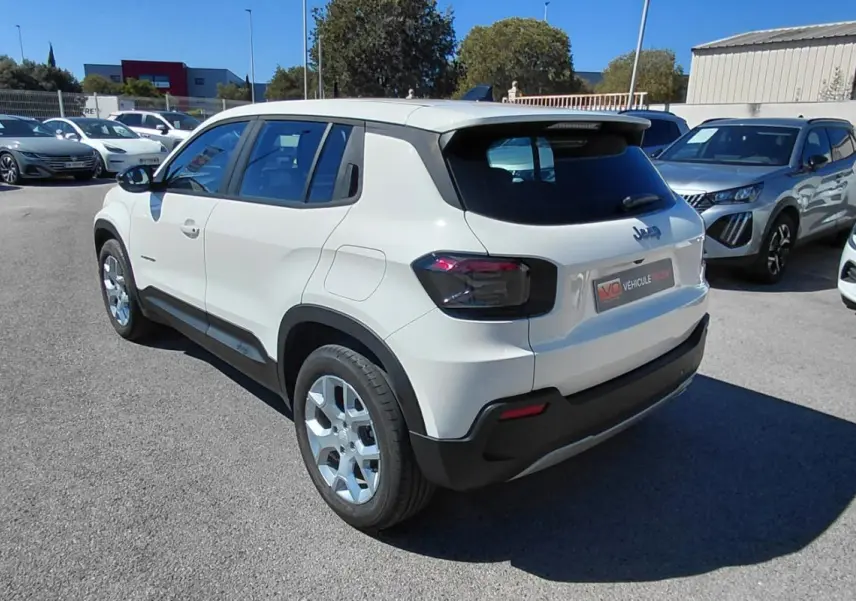 Jeep Avenger blanc en 3/4 arrière droit, avec feux arrière noirs et jantes argentées, stationné en extérieur.