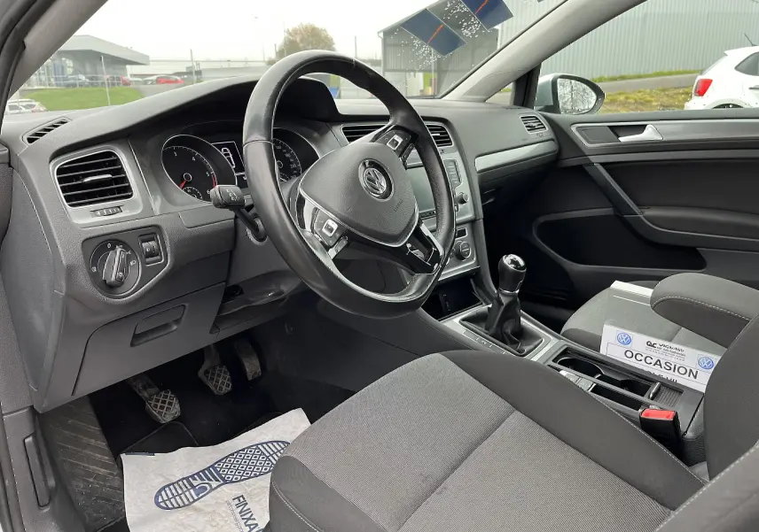 Intérieur noir de Volkswagen Golf 7 2017, vue côté conducteur montrant volant, tableau de bord et levier de vitesses manuel.