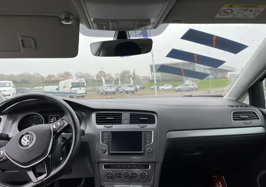 Vue intérieure avant du tableau de bord noir et volant Volkswagen d'une Golf 7 argent, avec écran tactile et commandes visibles.