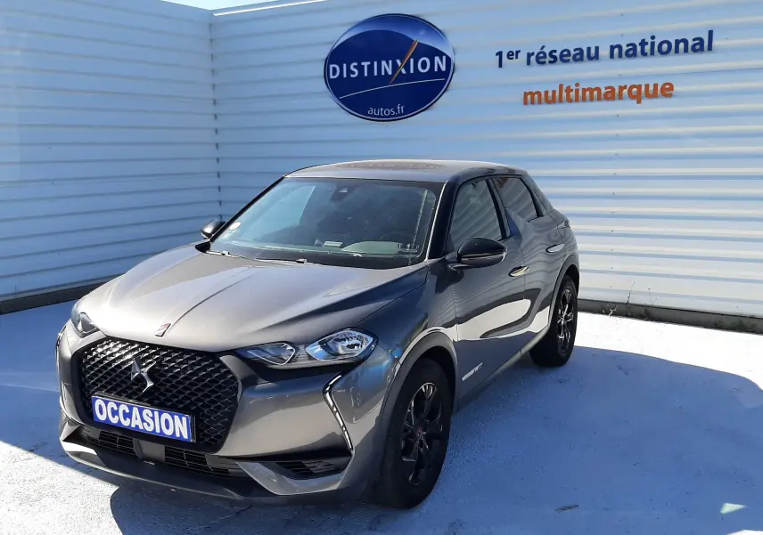DS3 Crossback gris foncé en 3/4 avant droit, avec calandre noire et jantes sombres, stationné devant un mur blanc.